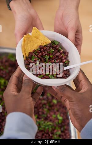 Vue verticale du dessus de la photo d'un volontaire méconnu donnant un bol avec repas à une personne en argent dans une cantine de charité Banque D'Images