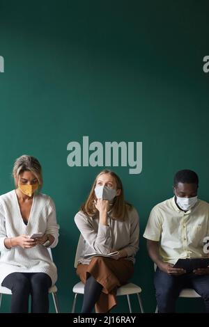 Groupe de personnes multiethniques modernes portant un masque protecteur attendant la lecture d'un entretien d'emploi, utilisant un smartphone et pensant à quelque chose Banque D'Images