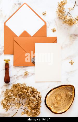 Ensemble de papeterie de mariage sur une table en marbre. Modèle de carte de vœux ou de mariage avec enveloppe en bronze, fleurs sèches, anneaux dorés, cachet de cire Banque D'Images