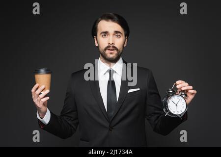 homme d'affaires avec moustache tenant une tasse en papier et un réveil sur gris foncé Banque D'Images