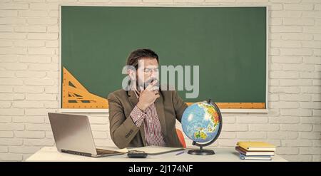 homme à barbe mature enseignant en costume assis dans la salle de classe avec géographie carte du globe, emplacement Banque D'Images