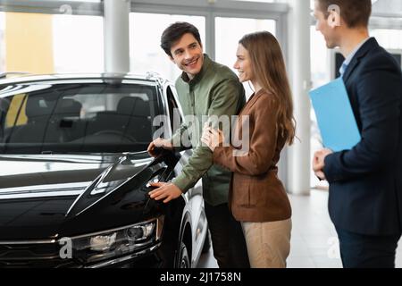 Achat ou location de voiture. Couple caucasien du millénaire parlant au vendeur au sujet de l'achat d'une nouvelle voiture à la concession Banque D'Images