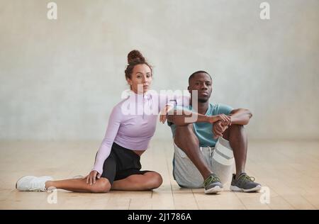 Photo en studio d'un jeune homme noir et d'une femme caucasienne sportif vêtu de tenues à la mode, assis au sol dans une chambre de studio loft avec vue sur l'appareil photo Banque D'Images