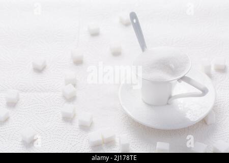 Sucre blanc granulé dans une tasse blanche avec cuillère sur fond blanc Banque D'Images
