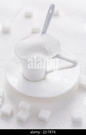 Sucre blanc granulé dans une tasse blanche avec cuillère sur fond blanc Banque D'Images