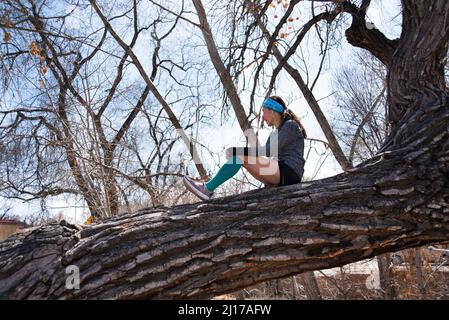 Une femme prend une pause de son exercice de jogging et repose dans un vieux arbre de coton torché à Santa Fe, Nouveau-Mexique. Banque D'Images