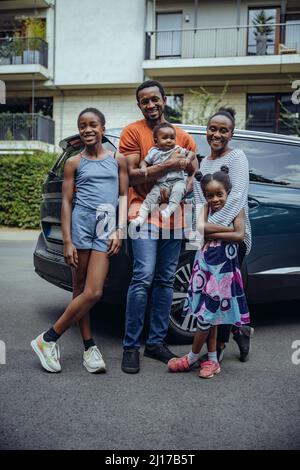 Famille souriante debout devant la voiture sur la route Banque D'Images