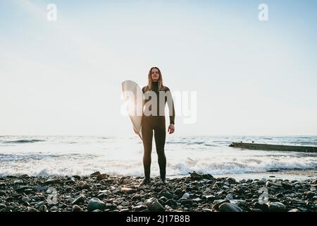 Homme debout sur une plage rocheuse avec surf Banque D'Images