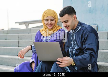 Jeune homme utilisant un ordinateur portable assis avec une femme sur un escalier Banque D'Images