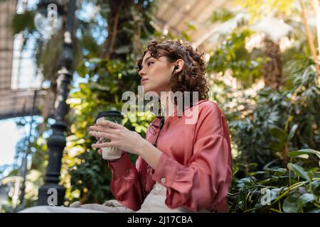 Femme contemplative avec du café jetable écoutant de la musique à travers des écouteurs Banque D'Images