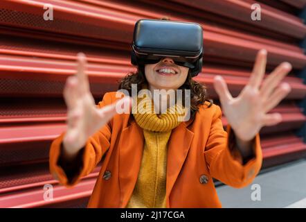 Jeune femme portant des lunettes VR devant un mur ondulé rouge Banque D'Images