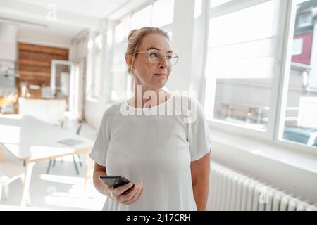 Femme d'affaires portant des lunettes tenant un smartphone au bureau Banque D'Images