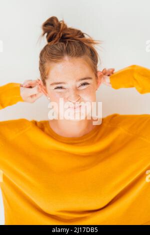 Jeune femme tirant les oreilles sur fond blanc Banque D'Images