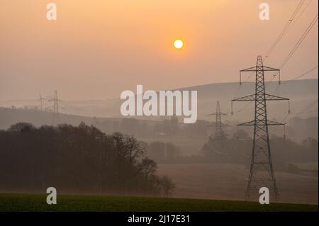 Ledgerwood aux frontières écossaises, Royaume-Uni. 23rd mars 2022. Engery, électricité, électricité. Le soleil se lève un autre jour de prix élevés de l'énergie alors que le coût de la vie continue d'augmenter. La transition vers l'énergie verte est une priorité, mais aussi l'équilibre entre la réduction des coûts de l'énergie actuellement élevée en raison de la pandémie de cavid et de la guerre actuelle en Ukraine et des sanctions contre la Russie. La vue est de pylônes d'électricité et une distance éolienne que le soleil se lève près de Ledgerwood dans les frontières écossaises. Crédit : phil wilkinson/Alay Live News Banque D'Images