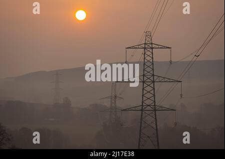 Ledgerwood aux frontières écossaises, Royaume-Uni. 23rd mars 2022. Engery, électricité, électricité. Le soleil se lève un autre jour de prix élevés de l'énergie alors que le coût de la vie continue d'augmenter. La transition vers l'énergie verte est une priorité, mais aussi l'équilibre entre la réduction des coûts de l'énergie actuellement élevée en raison de la pandémie de cavid et de la guerre actuelle en Ukraine et des sanctions contre la Russie. La vue est de pylônes d'électricité et une distance éolienne que le soleil se lève près de Ledgerwood dans les frontières écossaises. Crédit : phil wilkinson/Alay Live News Banque D'Images