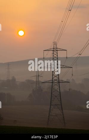 Ledgerwood aux frontières écossaises, Royaume-Uni. 23rd mars 2022. Engery, électricité, électricité. Le soleil se lève un autre jour de prix élevés de l'énergie alors que le coût de la vie continue d'augmenter. La transition vers l'énergie verte est une priorité, mais aussi l'équilibre entre la réduction des coûts de l'énergie actuellement élevée en raison de la pandémie de cavid et de la guerre actuelle en Ukraine et des sanctions contre la Russie. La vue est de pylônes d'électricité et une distance éolienne que le soleil se lève près de Ledgerwood dans les frontières écossaises. Crédit : phil wilkinson/Alay Live News Banque D'Images