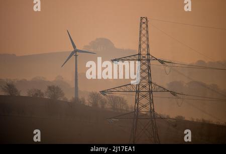 Ledgerwood aux frontières écossaises, Royaume-Uni. 23rd mars 2022. Engery, électricité, électricité. Le soleil se lève un autre jour de prix élevés de l'énergie alors que le coût de la vie continue d'augmenter. La transition vers l'énergie verte est une priorité, mais aussi l'équilibre entre la réduction des coûts de l'énergie actuellement élevée en raison de la pandémie de cavid et de la guerre actuelle en Ukraine et des sanctions contre la Russie. La vue est de pylônes d'électricité et une distance éolienne que le soleil se lève près de Ledgerwood dans les frontières écossaises. Crédit : phil wilkinson/Alay Live News Banque D'Images