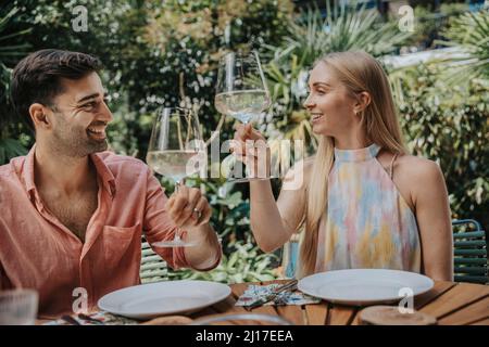 Couple souriant en train de griller des verres à vin à la table extérieure Banque D'Images