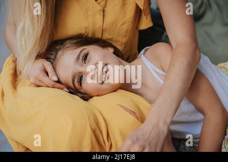 Fille souriante couchée sur les genoux de la mère dans le patio Banque D'Images