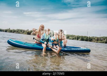 Famille gaie avec paddleboard dans le lac le week-end Banque D'Images