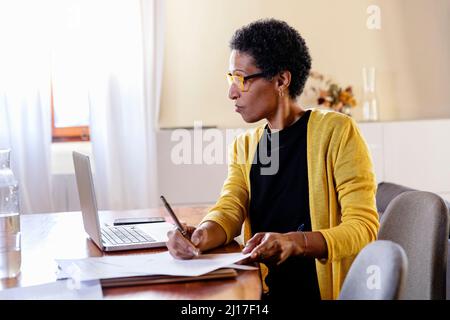 Femme d'affaires regardant un ordinateur portable et faisant de la paperasserie dans le bureau à domicile Banque D'Images