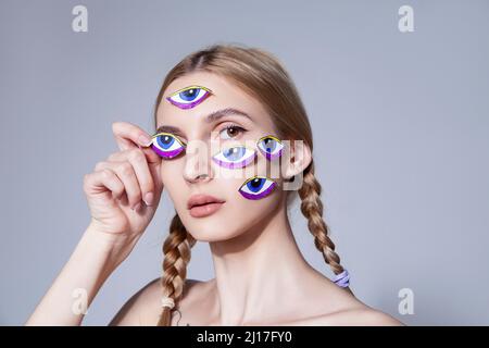 Jeune femme avec des cheveux tressés avec des autocollants pour les yeux sur le visage au studio Banque D'Images