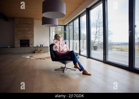 Femme assise sur une chaise dans la salle de séjour à la maison Banque D'Images