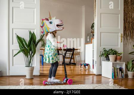 Fille avec masque unicorn équitation pousser scooter à la maison Banque D'Images