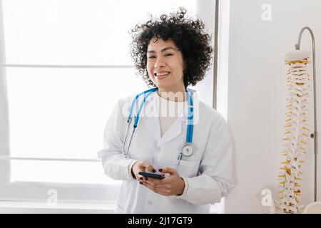 Un jeune médecin heureux tenant un smartphone près de la fenêtre à la clinique Banque D'Images