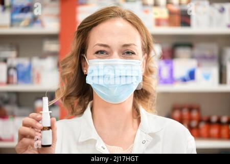 Une pharmacienne portant un masque facial de protection contenant un flacon de vaporisateur nasal dans un magasin de pharmacie Banque D'Images