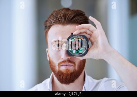Jeune homme regardant à travers l'objectif de caméra ouverte au bureau Banque D'Images