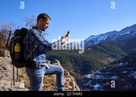 Randonneur avec sac à dos pour photographier à travers un smartphone debout sur le rocher Banque D'Images