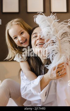 Bonne mère et fille jouant avec la plume à la maison Banque D'Images