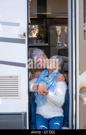 Homme âgé embrassant la femme heureuse sur la joue assis à la porte de la maison de moteur Banque D'Images