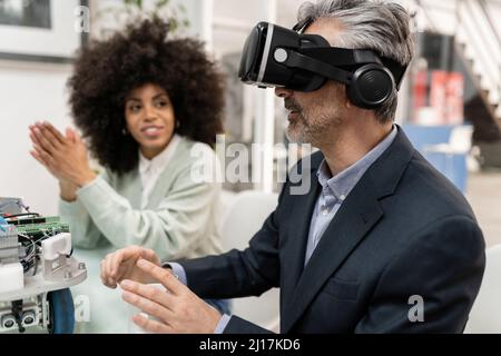 Homme d'affaires portant un simulateur de réalité virtuelle assis par un collègue en usine Banque D'Images