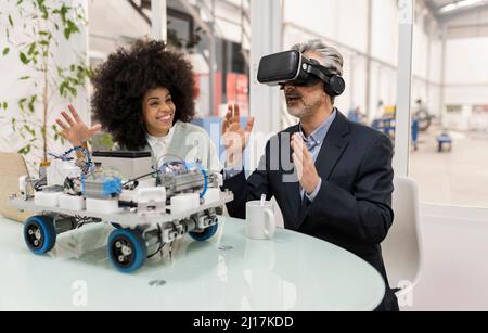Développeur souriant regardant un homme d'affaires portant un simulateur de réalité virtuelle en usine Banque D'Images