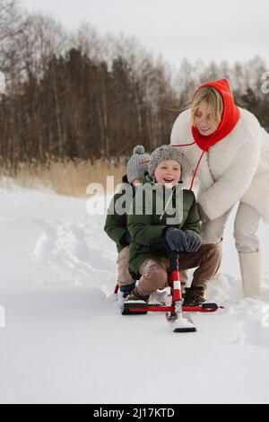 Bonne mère poussant des fils assis sur un toboggan en hiver Banque D'Images