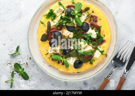 Œufs brouillés. Des œufs brouillés légers, doux et Buttery avec fromage feta, tomates séchées et olives noires sur plaque sur fond de pierre blanche. D Banque D'Images