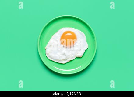 Un œuf frit dans une assiette minimaliste sur une table verte. Vue de dessus avec un œuf frit isolé sur un fond coloré. Banque D'Images