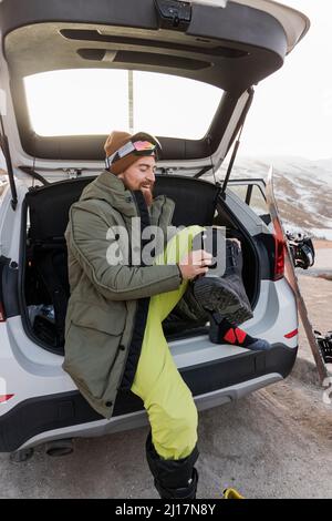 Jeune homme souriant dans le coffre de voiture se préparant pour le snowboard Banque D'Images