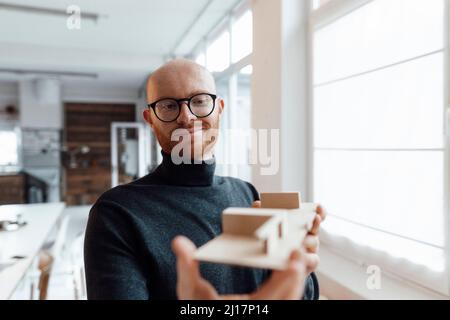 Un jeune homme d'affaires souriant examine un modèle en bois au bureau Banque D'Images