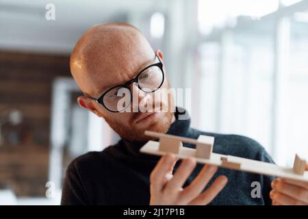 Un jeune homme d'affaires examine un modèle en bois au bureau Banque D'Images