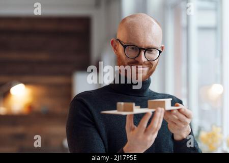 Jeune homme d'affaires souriant avec un modèle en bois au bureau Banque D'Images