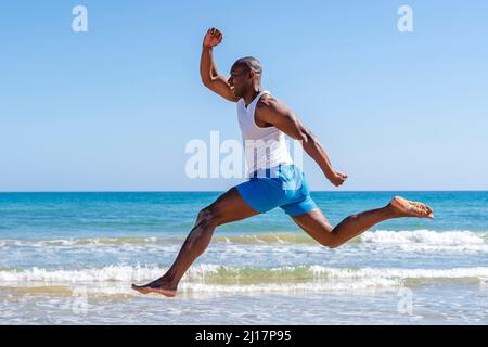 Un athlète souriant sautant devant l'eau à la plage par beau temps Banque D'Images