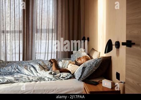Homme dormant sur un lit confortable le matin à la maison Banque D'Images
