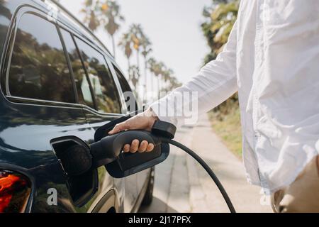 Homme qui branche le cordon de charge dans la voiture électrique sur la route à la station Banque D'Images