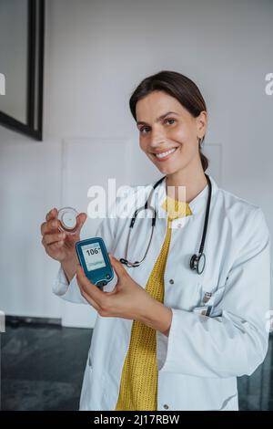 Médecin souriant tenant le glucomètre dans la clinique Banque D'Images