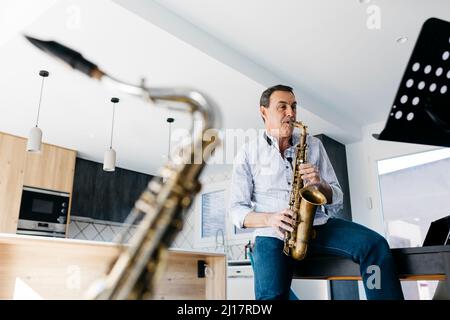 Saxophoniste jouant du saxophone assis sur une table à la maison Banque D'Images