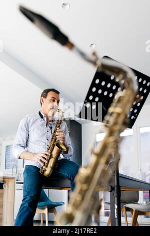 Musicien jouant du saxophone assis sur une table à la maison Banque D'Images