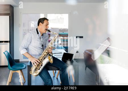 Saxophoniste soufflant saxophone assis sur une table à la maison Banque D'Images